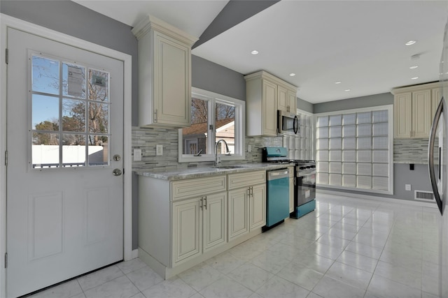 kitchen with sink, decorative backsplash, cream cabinetry, light stone counters, and stainless steel appliances