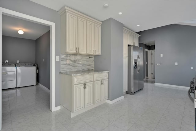 kitchen with separate washer and dryer, stainless steel fridge with ice dispenser, light stone counters, and cream cabinetry