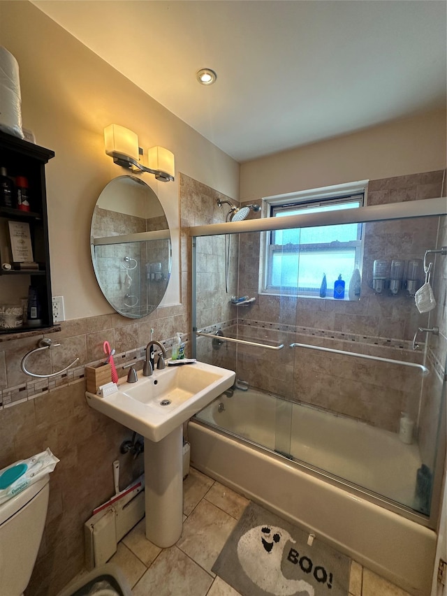 bathroom featuring tile patterned floors, toilet, bath / shower combo with glass door, and tile walls