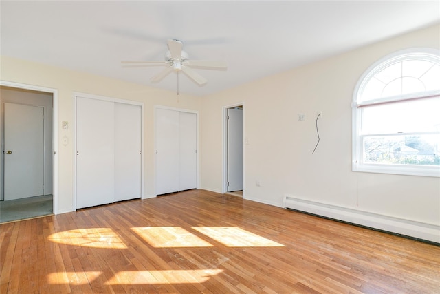 unfurnished bedroom with ceiling fan, light hardwood / wood-style flooring, two closets, and a baseboard heating unit