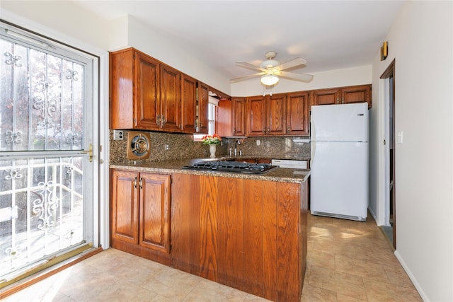 kitchen with white refrigerator, ceiling fan, kitchen peninsula, backsplash, and black gas stovetop