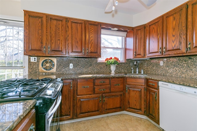 kitchen with dark stone countertops, stainless steel gas stove, white dishwasher, a wealth of natural light, and sink