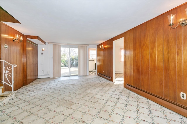 empty room with wooden walls, a baseboard radiator, and light carpet