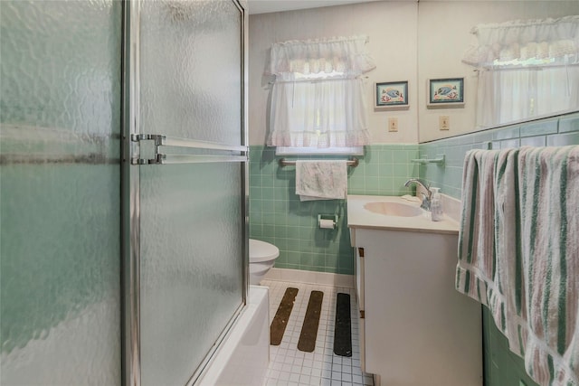 full bathroom with tile patterned floors, toilet, shower / bath combination with glass door, vanity, and tile walls