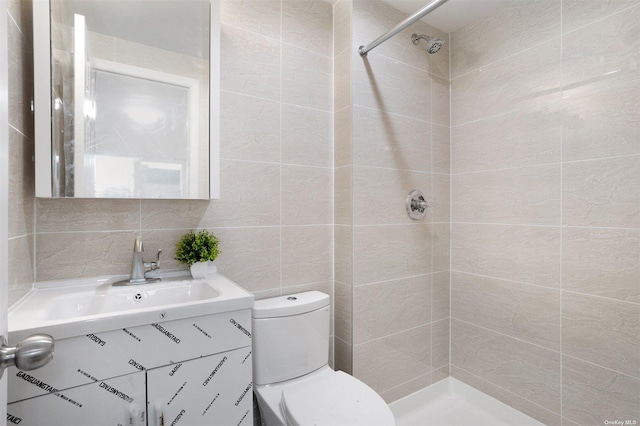 bathroom with a tile shower, vanity, toilet, and tile walls