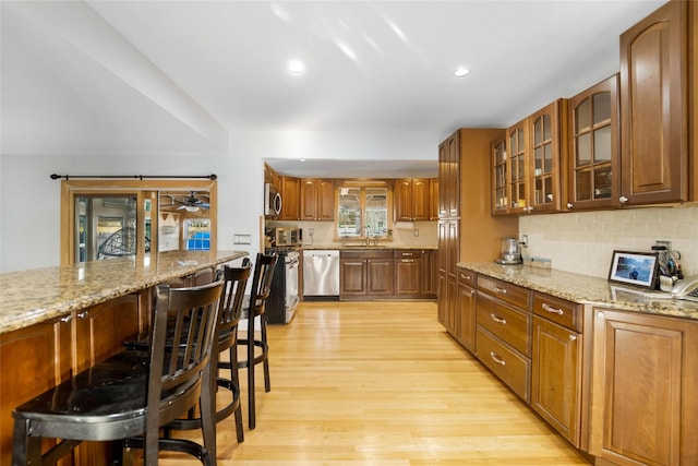 kitchen with a breakfast bar area, stainless steel appliances, light hardwood / wood-style floors, and light stone counters