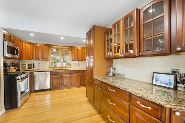 kitchen with tasteful backsplash, sink, light wood-type flooring, light stone countertops, and stainless steel appliances