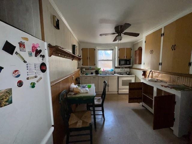 kitchen with white appliances, ceiling fan, crown molding, and wood walls