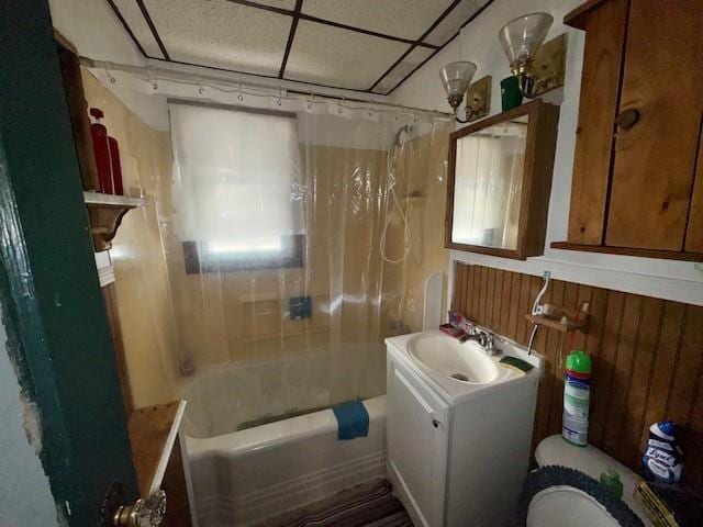 bathroom with shower / bath combo, vanity, wooden walls, and a paneled ceiling