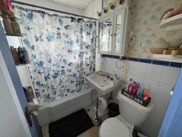 full bathroom featuring sink, toilet, shower / bath combo with shower curtain, and tile walls