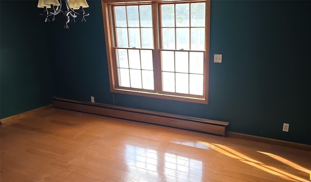 unfurnished room featuring light hardwood / wood-style flooring, a baseboard heating unit, and a notable chandelier