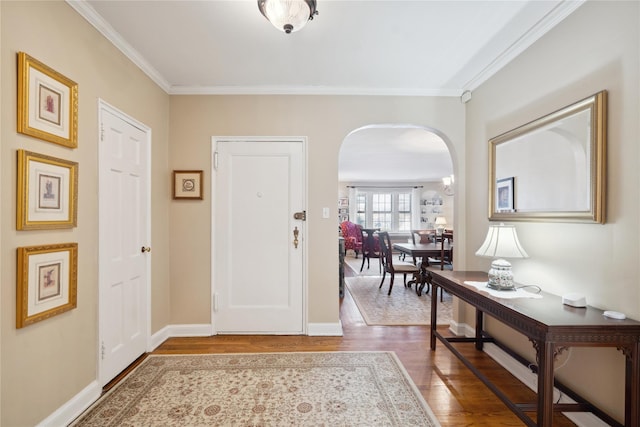 entryway featuring baseboards, arched walkways, wood finished floors, and ornamental molding