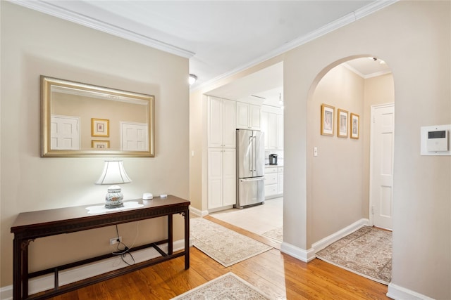 hall featuring arched walkways, light wood-type flooring, baseboards, and crown molding