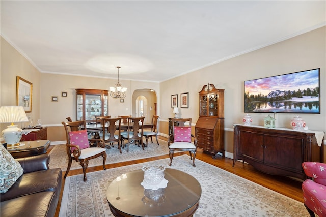 living room featuring arched walkways, a notable chandelier, wood finished floors, baseboards, and ornamental molding