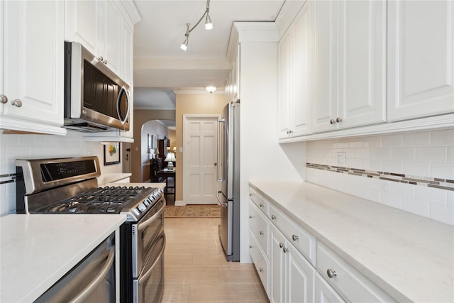 kitchen featuring stainless steel appliances, arched walkways, white cabinetry, and ornamental molding