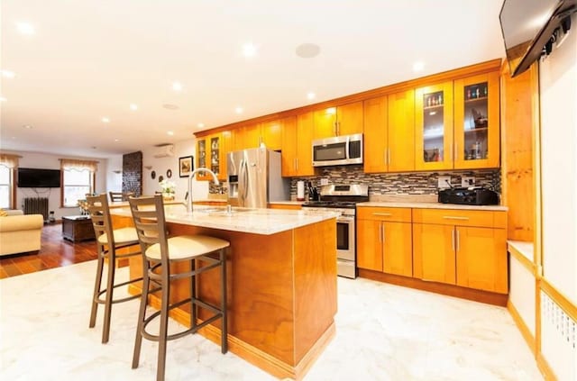 kitchen with a kitchen island with sink, sink, a breakfast bar area, light stone counters, and stainless steel appliances