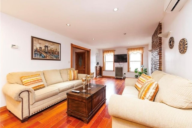 living room with a wall mounted air conditioner, hardwood / wood-style floors, and radiator