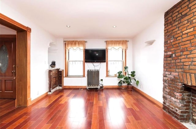 unfurnished living room featuring radiator, a fireplace, and wood-type flooring