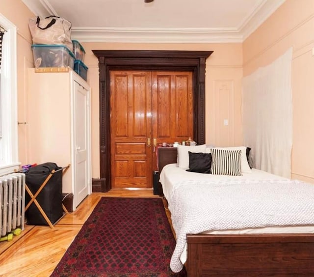 bedroom featuring light wood-type flooring, radiator heating unit, and ornamental molding