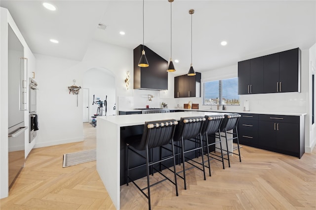 kitchen with hanging light fixtures, light parquet flooring, a kitchen island, a kitchen breakfast bar, and sink