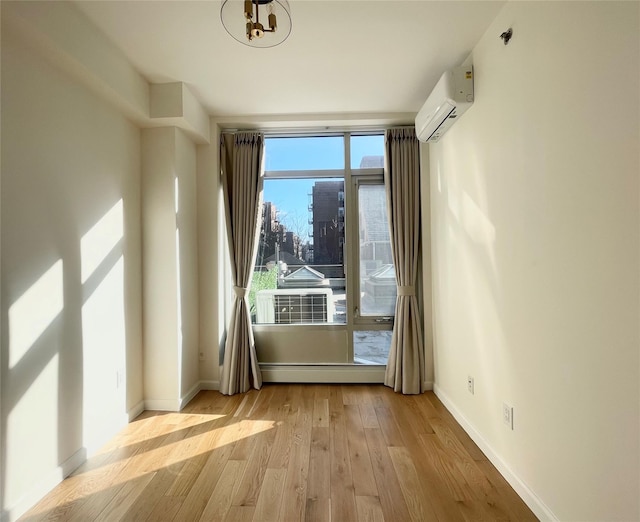 unfurnished room with a baseboard heating unit, an AC wall unit, light hardwood / wood-style flooring, and a wealth of natural light