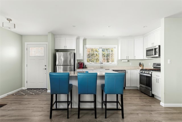 kitchen featuring a kitchen island, a breakfast bar, white cabinets, stainless steel appliances, and light hardwood / wood-style flooring