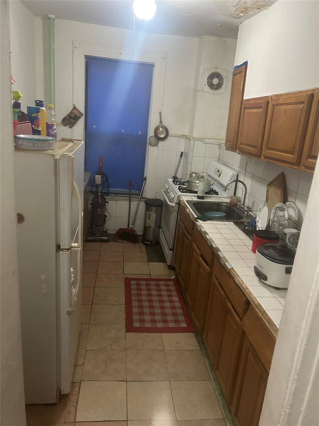 kitchen featuring tile counters, sink, backsplash, white appliances, and light tile patterned floors