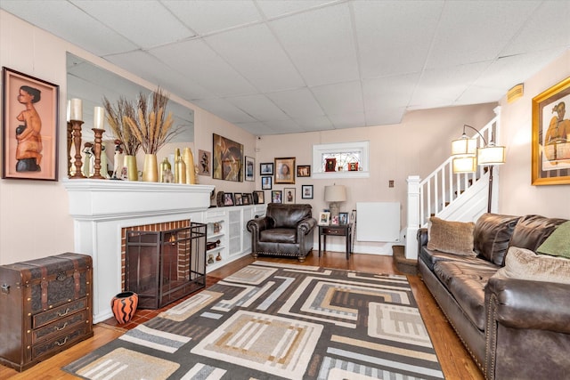 living room with a paneled ceiling, a brick fireplace, and hardwood / wood-style flooring