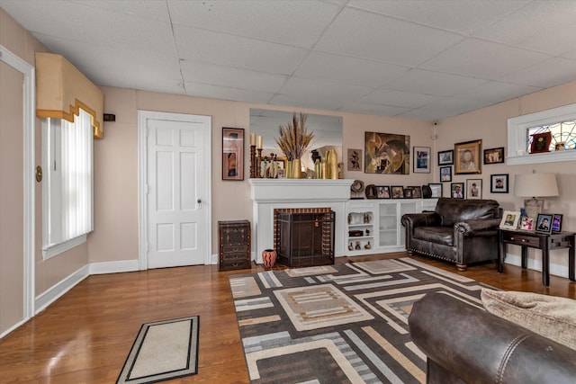 living room featuring a paneled ceiling, wood-type flooring, and a brick fireplace