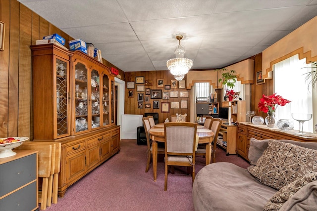 carpeted dining area featuring an inviting chandelier and wood walls