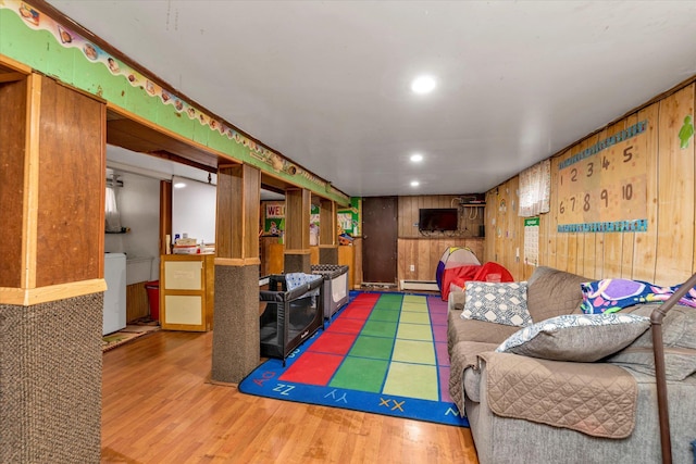 living room with hardwood / wood-style floors, wood walls, washer / dryer, and a baseboard radiator