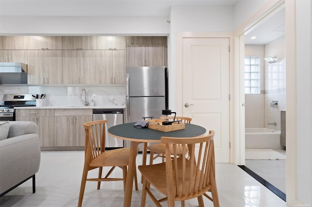 kitchen with sink, stainless steel appliances, decorative backsplash, light brown cabinetry, and light tile patterned flooring