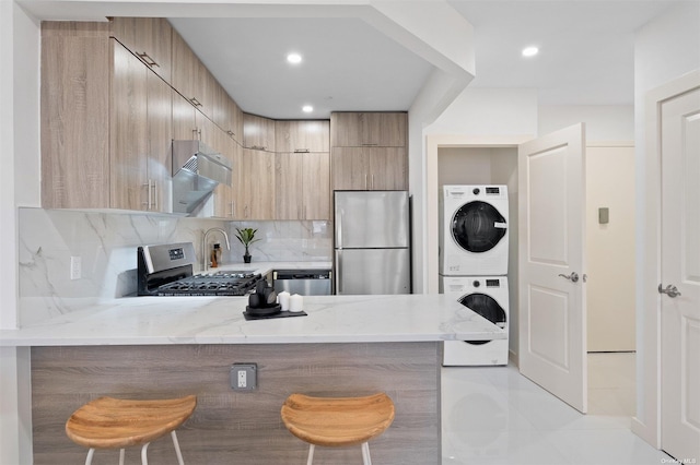 kitchen featuring tasteful backsplash, kitchen peninsula, stacked washer / drying machine, a breakfast bar, and appliances with stainless steel finishes