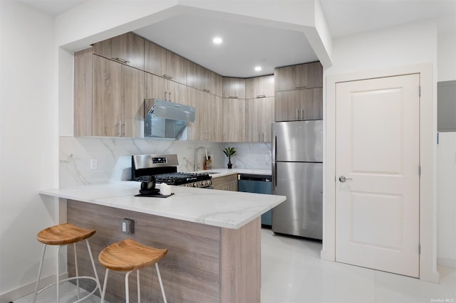 kitchen featuring a breakfast bar, light stone countertops, appliances with stainless steel finishes, and tasteful backsplash