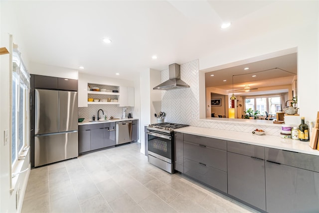 kitchen with gray cabinetry, sink, wall chimney exhaust hood, backsplash, and appliances with stainless steel finishes