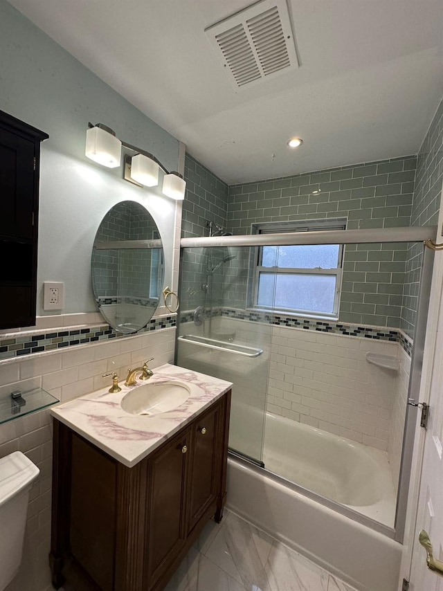 bathroom featuring combined bath / shower with glass door, vanity, tasteful backsplash, and tile walls