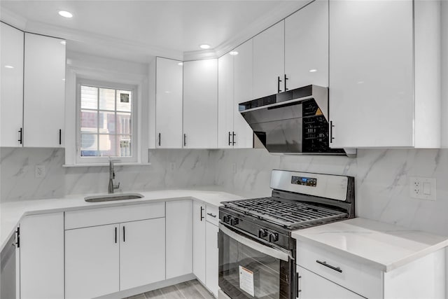 kitchen with gas range, sink, light stone counters, decorative backsplash, and white cabinets