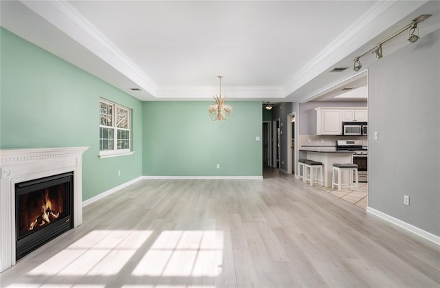 unfurnished living room featuring an inviting chandelier, a raised ceiling, ornamental molding, and light hardwood / wood-style floors