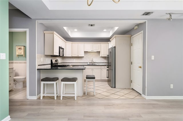 kitchen with sink, dark stone countertops, a tray ceiling, a kitchen bar, and appliances with stainless steel finishes