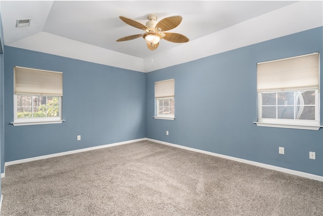 empty room featuring a raised ceiling, ceiling fan, carpet floors, and vaulted ceiling