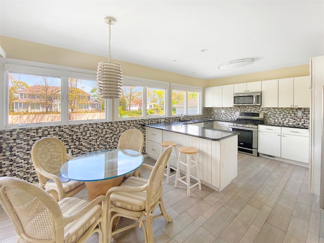 kitchen with appliances with stainless steel finishes, a kitchen breakfast bar, tasteful backsplash, decorative light fixtures, and white cabinetry