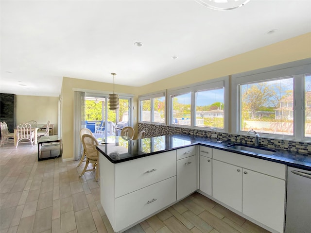 kitchen featuring dishwasher, sink, backsplash, pendant lighting, and white cabinets