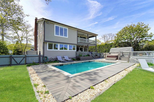 back of property featuring a lawn, a balcony, and a pool with hot tub