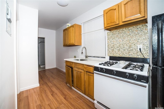 kitchen with white gas range, sink, black fridge, light hardwood / wood-style flooring, and decorative backsplash