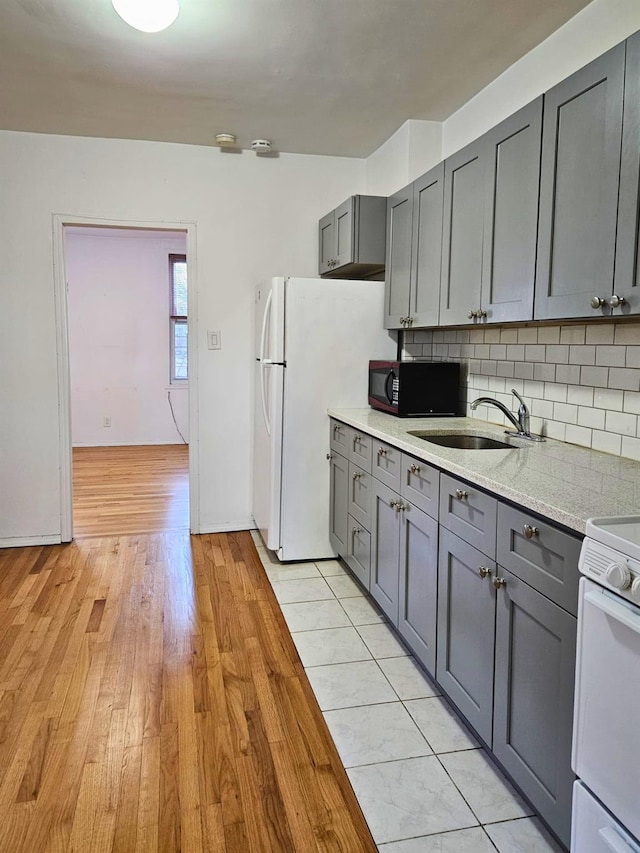 kitchen featuring sink, gray cabinetry, decorative backsplash, white appliances, and light hardwood / wood-style flooring