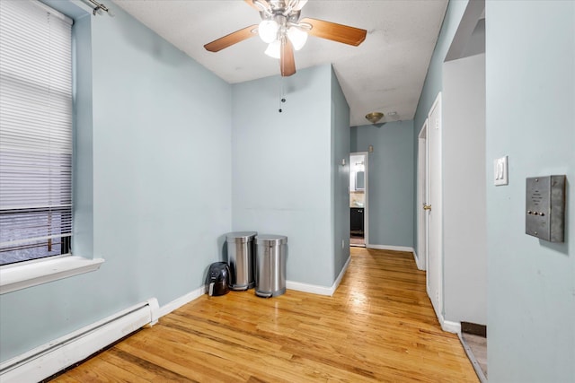 unfurnished room with a baseboard heating unit, light wood-type flooring, and ceiling fan