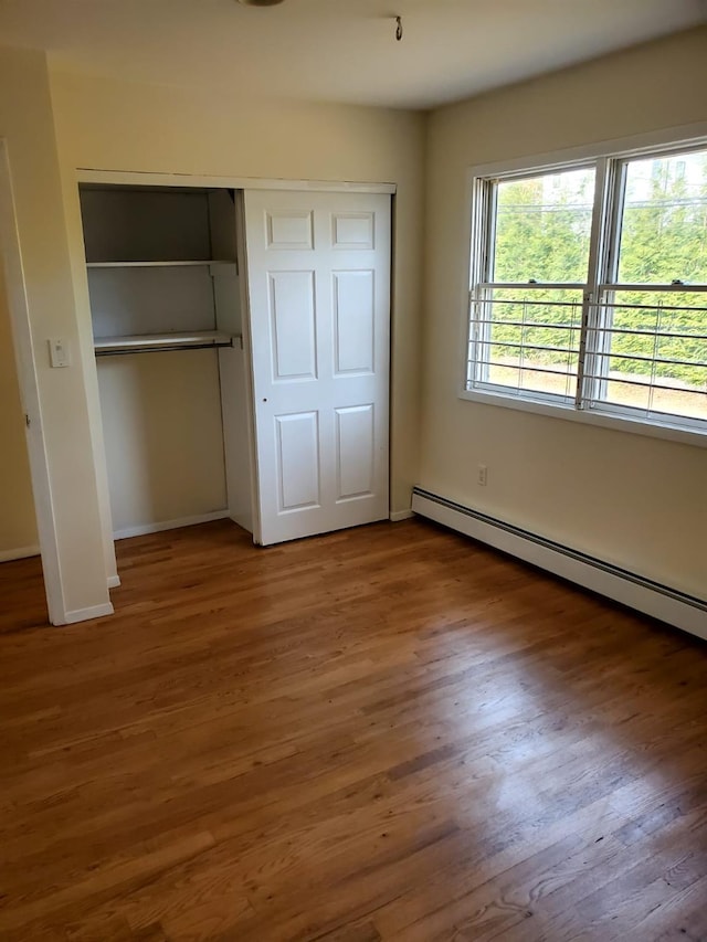 unfurnished bedroom with dark hardwood / wood-style floors and a baseboard heating unit