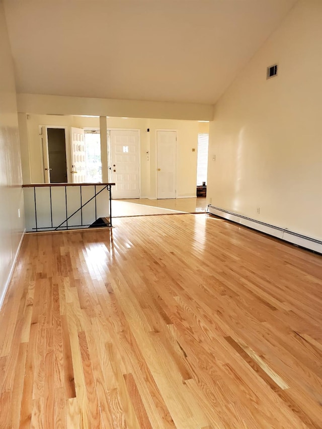 spare room featuring light wood-type flooring, baseboard heating, and vaulted ceiling