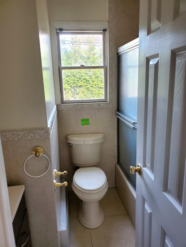 full bathroom with tile patterned flooring, bath / shower combo with glass door, toilet, vanity, and tile walls