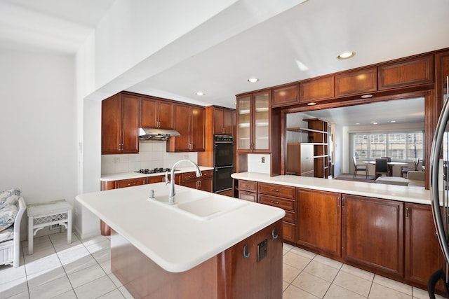 kitchen featuring light tile patterned flooring, a center island with sink, double oven, and sink